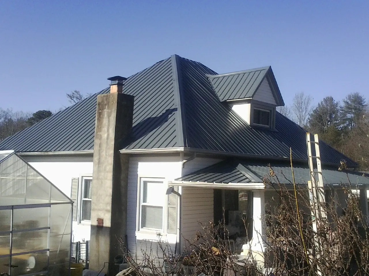 Dark blue standing seam metal roof on a white farmhouse with dormer — Slate & Tile Roof Repair by Roofing Brothers in Pleasant Garden