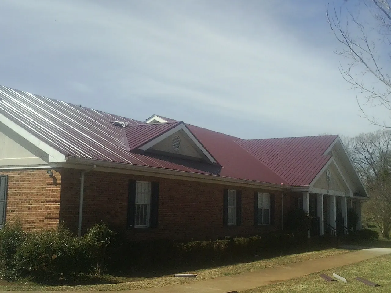 Red metal roof with gabled entries on a long brick building, from a Hail Damage Roof Repair job in Pleasant Garden
