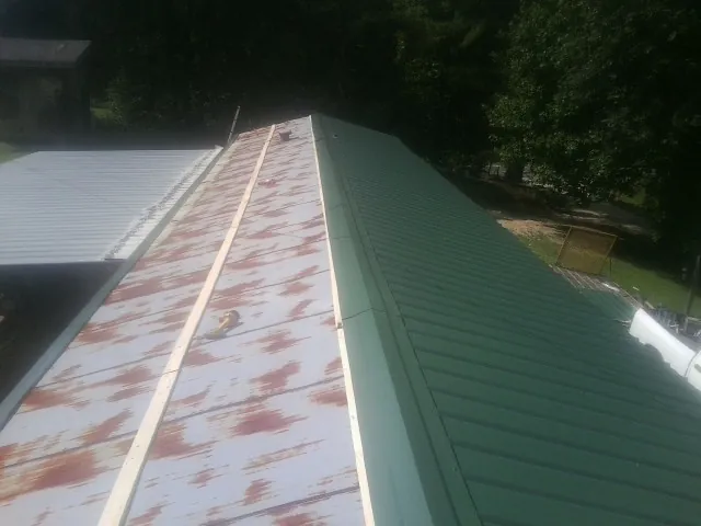 Old rusted panels beside newly installed green metal roofing — Wind Damage Roof Repair by Roofing Brothers in Pleasant Garden