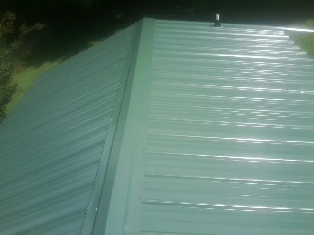 New green metal panels meeting at the ridge of a roof — Flat Roof Repair work by our crew in Pleasant Garden