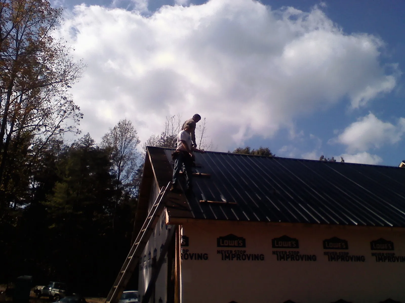 Roofer fastening dark metal panels high against a cloudy sky, from a Roof Inspection job in Pleasant Garden