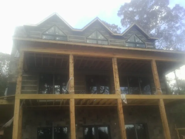 Dormers and porch framing on a large log home under construction — Roof Coating work by our crew in Pleasant Garden
