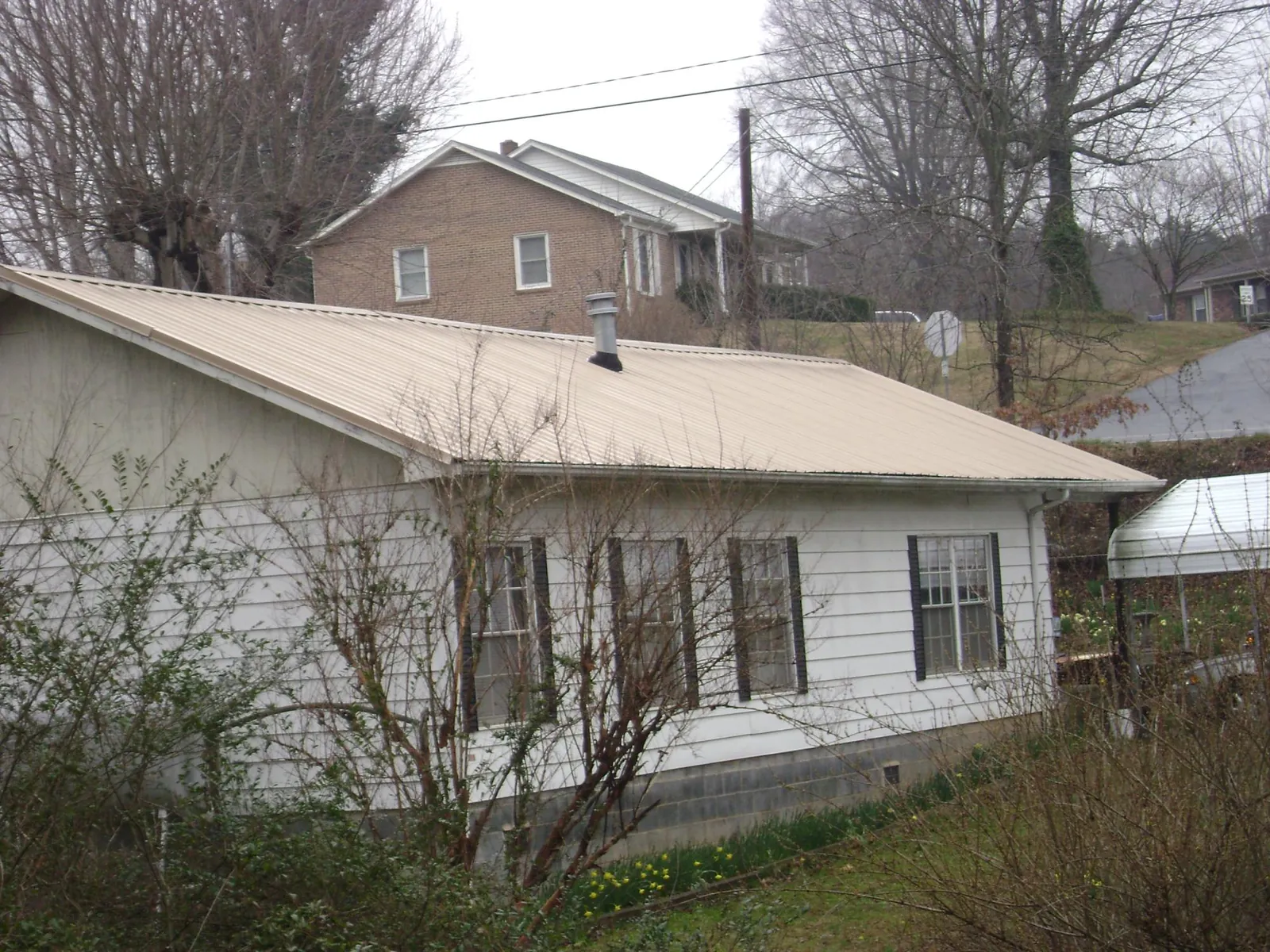 Tan metal roof on a white sided house set into a hillside — Commercial Roofing by Roofing Brothers in Pleasant Garden
