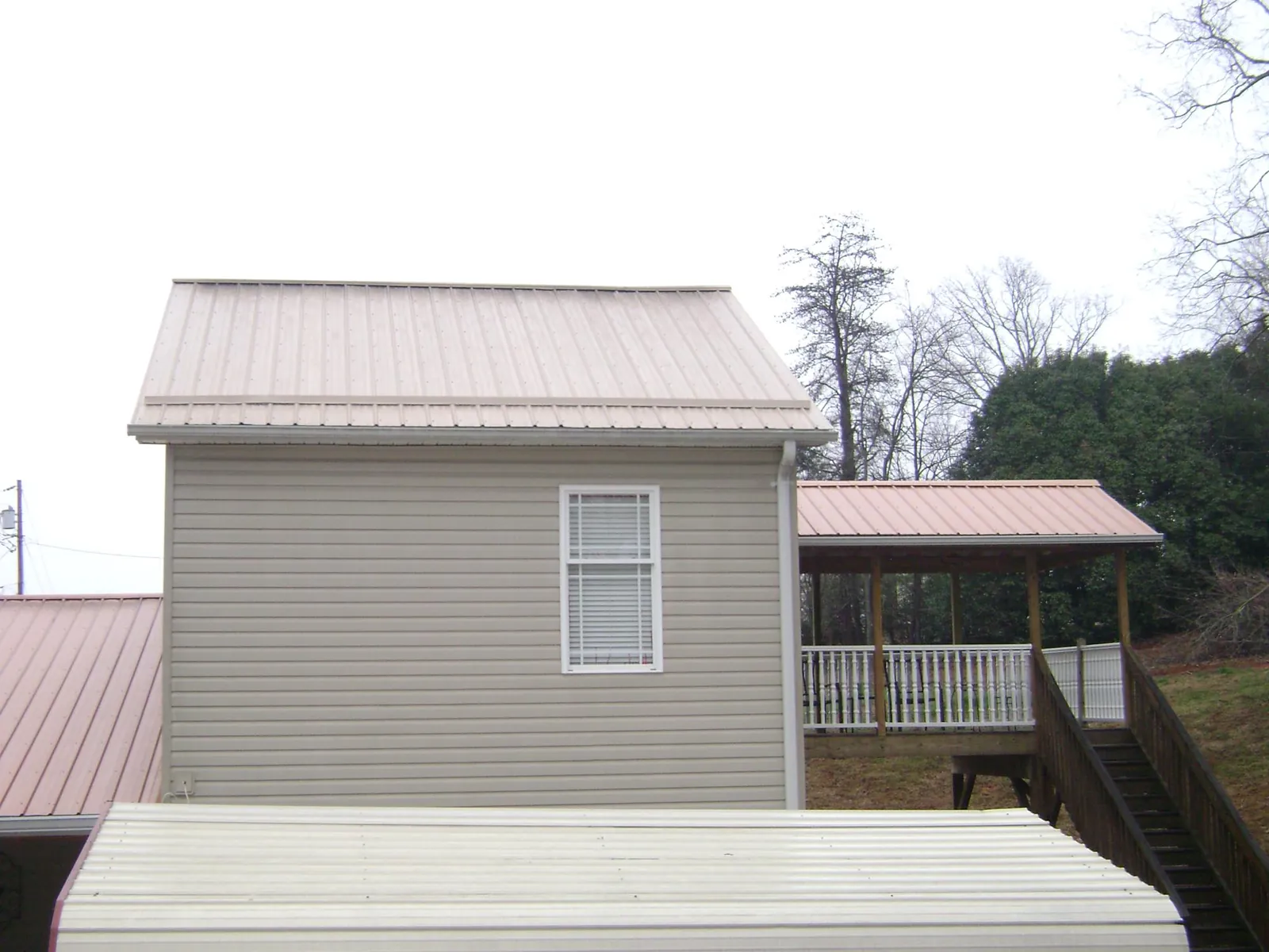 Tan metal roofs on a two story addition and attached porch, from a Roof Replacement job in Pleasant Garden